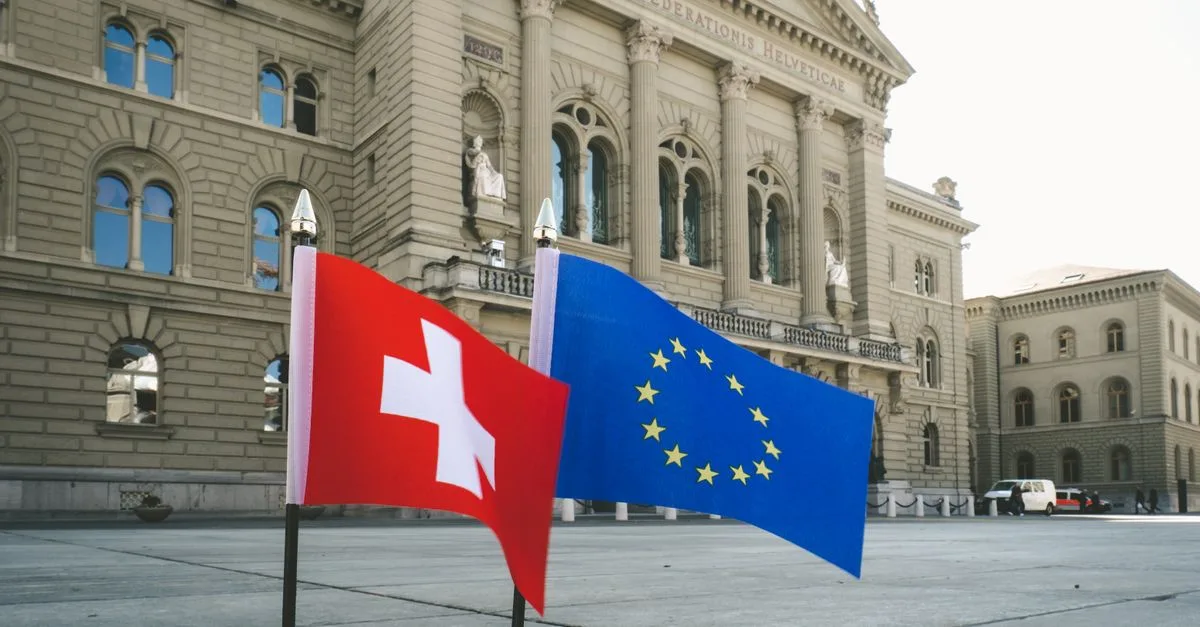 Front view of Swiss Parliament Building in Bern with Swiss and EU flags.