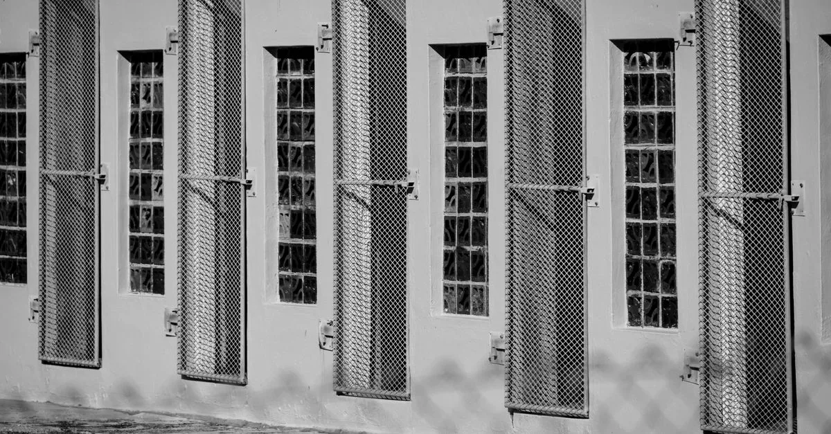 Monochrome image of barred windows on a building, depicting confinement and security.