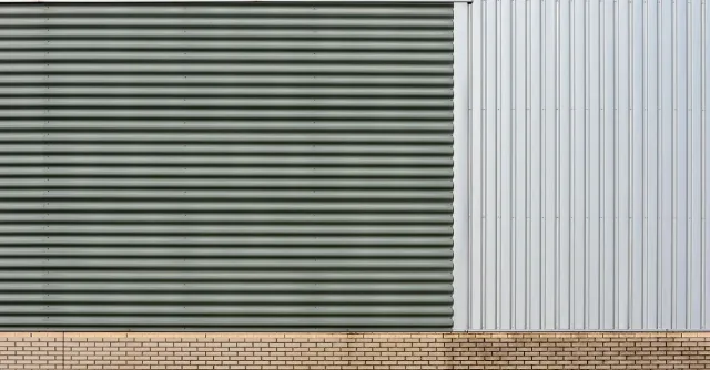 Close-up of industrial building facade with metal siding and brick base, showcasing slick and modern design.