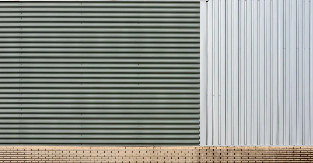 Close-up of industrial building facade with metal siding and brick base, showcasing slick and modern design.