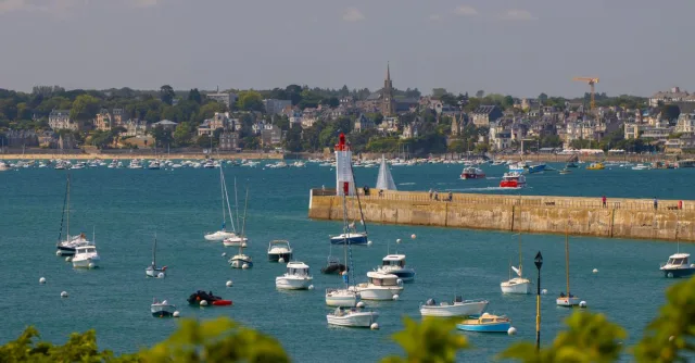 Picturesque view of Saint-Malo harbor with sailboats and a lighthouse under a clear sky.
