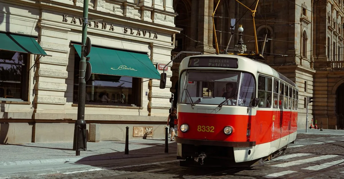 Red tram passes by historic buildings in Prague's city center on a sunny day.