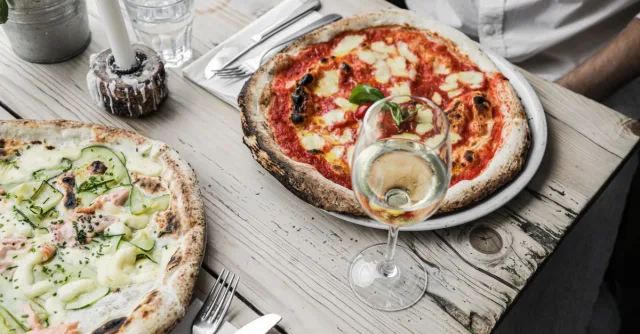 Appetizing pizzas with white wine served on a rustic wooden table, perfect for culinary enthusiasts.