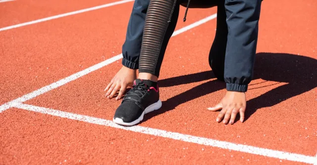 Close-up of a runner crouching at the starting line on an outdoor track.
