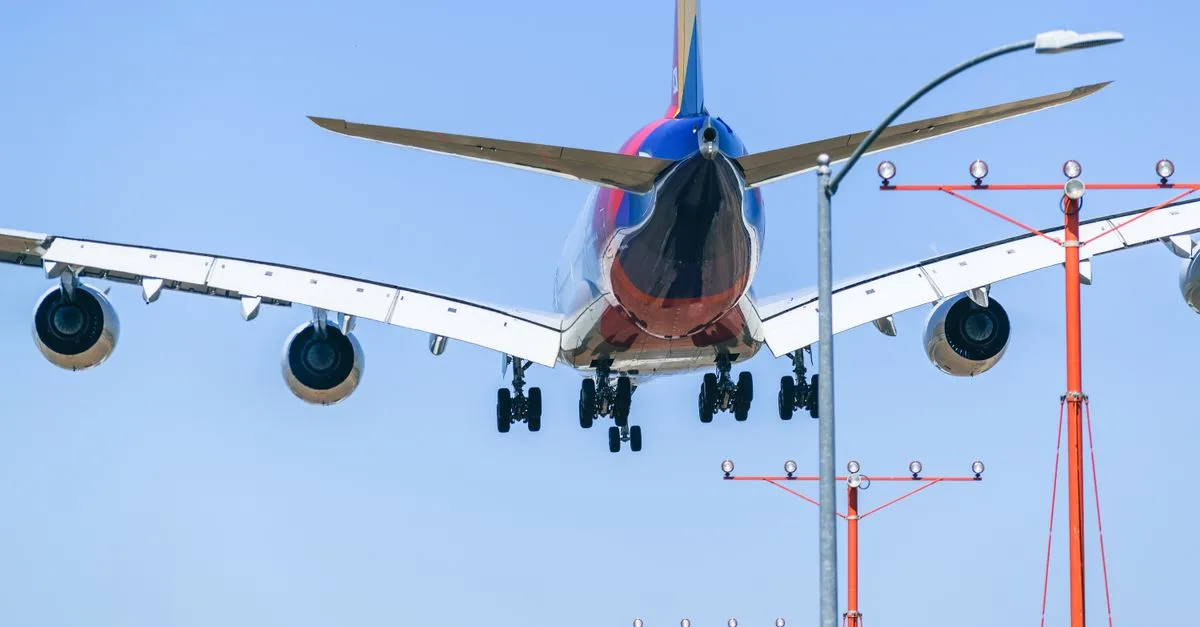 Passenger airplane approaching runway during daytime landing with clear blue sky backdrop.