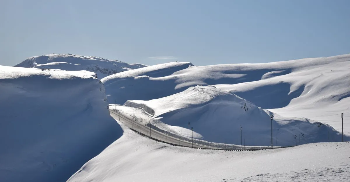 A stunning view of a winding road through snow-covered mountains in Norway during winter.
