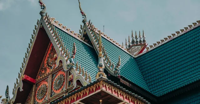 From below of bright ornamental roof with pointed peaks of aged Asian church under cloudy sky
