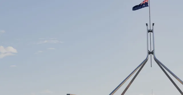 Canberra's iconic Australian Parliament House with national flag against a clear blue sky.
