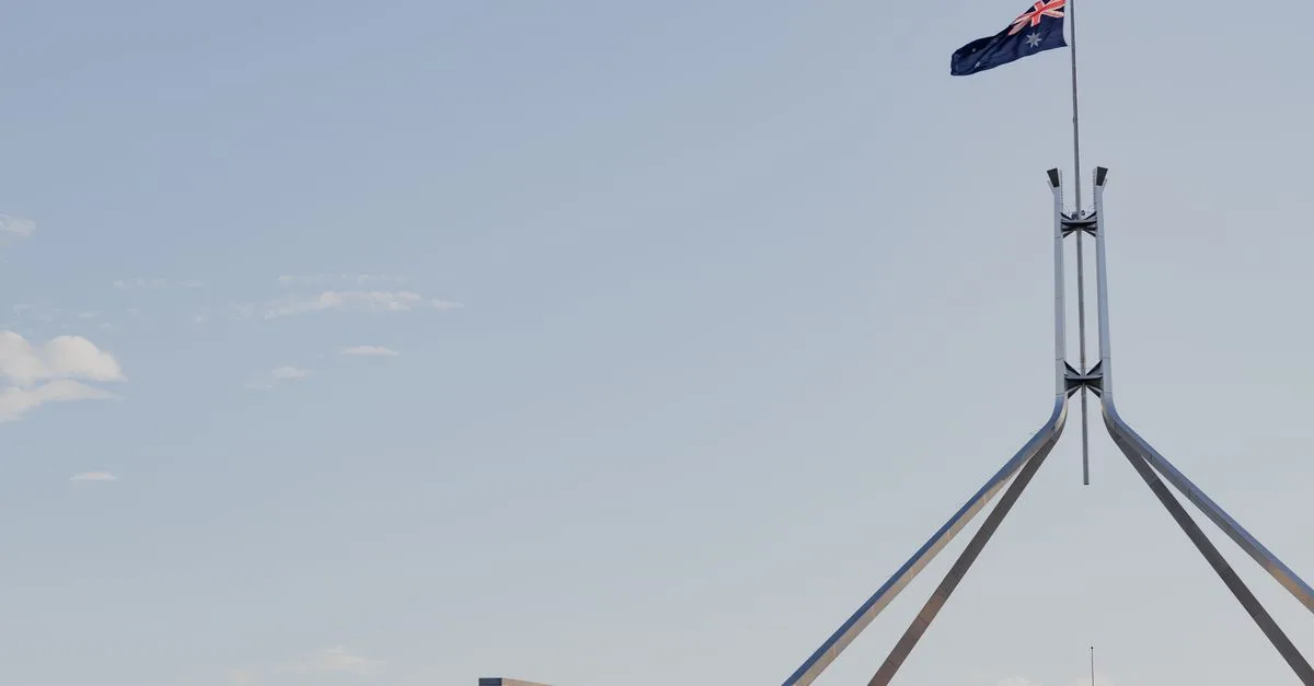 Canberra's iconic Australian Parliament House with national flag against a clear blue sky.