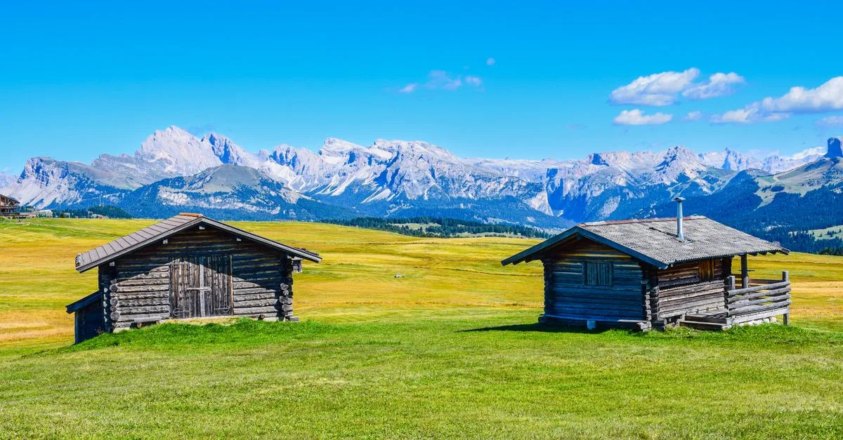 Charming wooden cabins set against stunning mountain backdrop in tranquil alpine meadow.