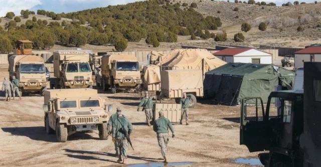 Military vehicles and tents at a training camp in Afghanistan under clear skies.