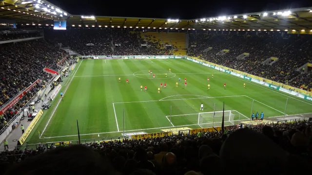 Ein beleuchtetes Fußballstadion bei Nacht mit Blick auf das Spielfeld.
