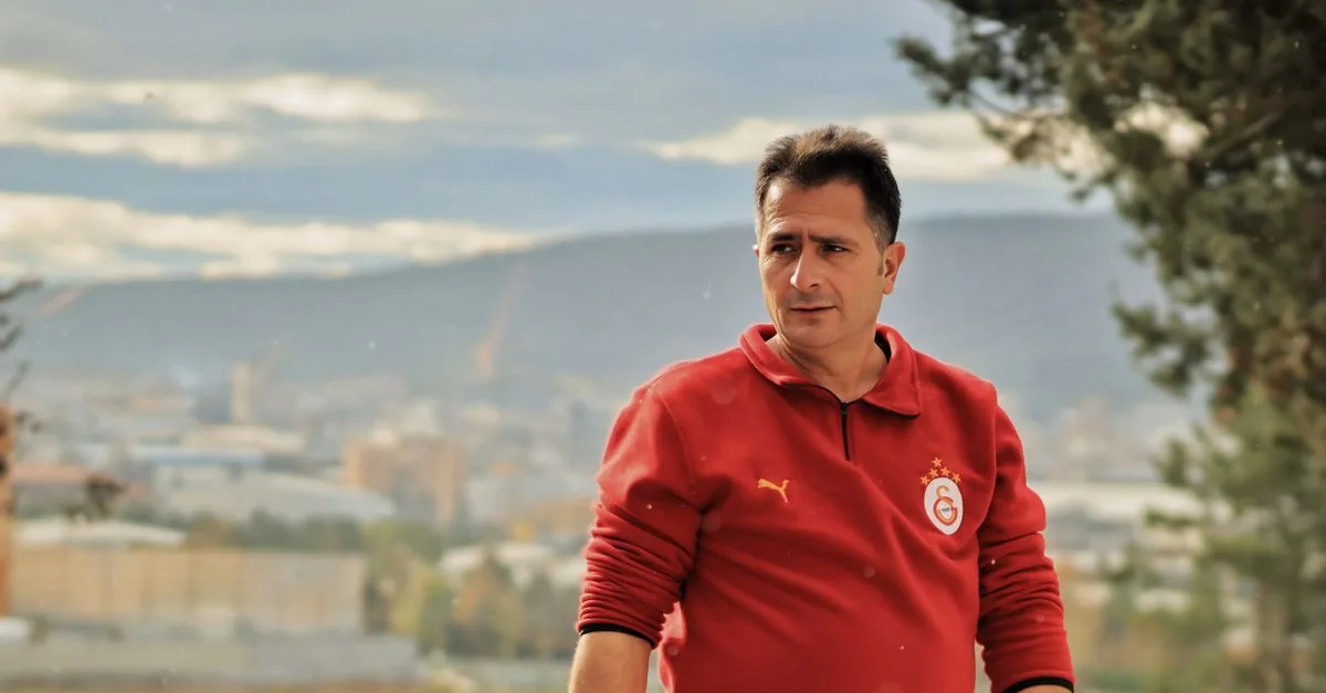Man in red sweatshirt with city skyline in background, shot outdoors.