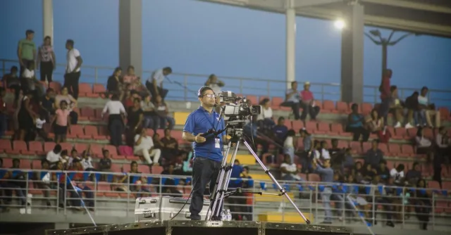 Cameraman on platform capturing footage at crowded stadium event.