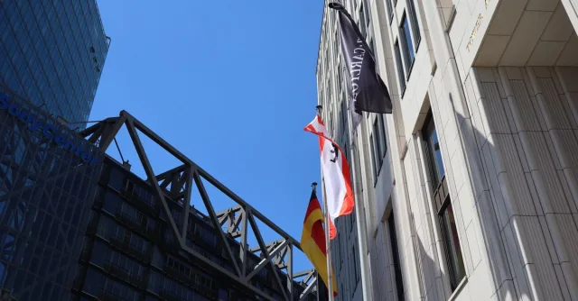 Low angle view of modern buildings in Berlin with flags against blue sky.