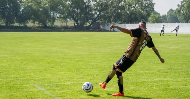 Adult male soccer player kicking a ball during training on a sunny day.