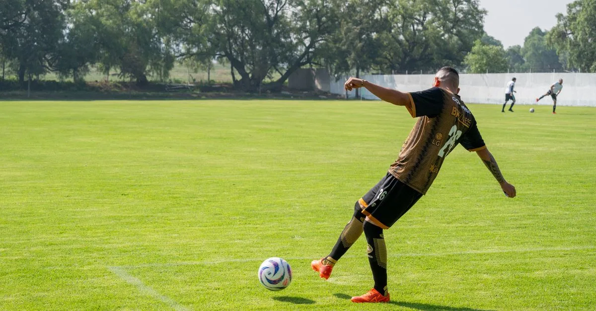 Adult male soccer player kicking a ball during training on a sunny day.