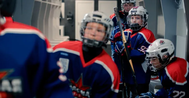 Young hockey team members in gear preparing for a match in the locker room.