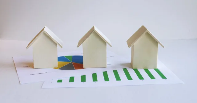 Wooden model houses on graphs depict real estate market analysis and trends.