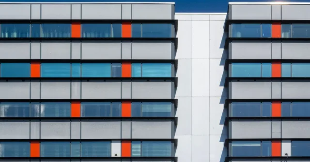 Contemporary building facade with red and gray panels under clear blue sky.