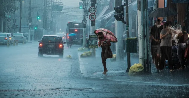 A busy urban street during heavy rain, with cars, pedestrians, and umbrellas.