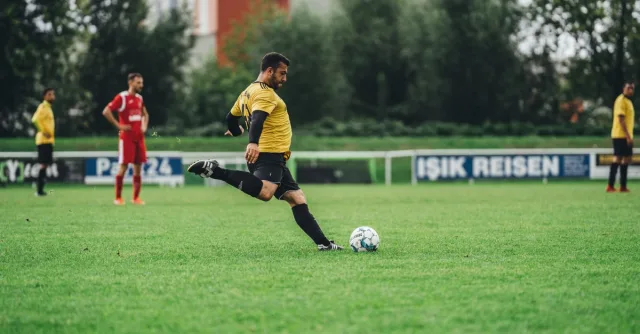 A soccer player in yellow uniform kicks a ball during a game on a green outdoor field.