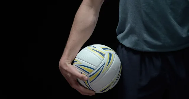 Close-up shot of a volleyball held by a person against a dark background, emphasizing sports readiness.