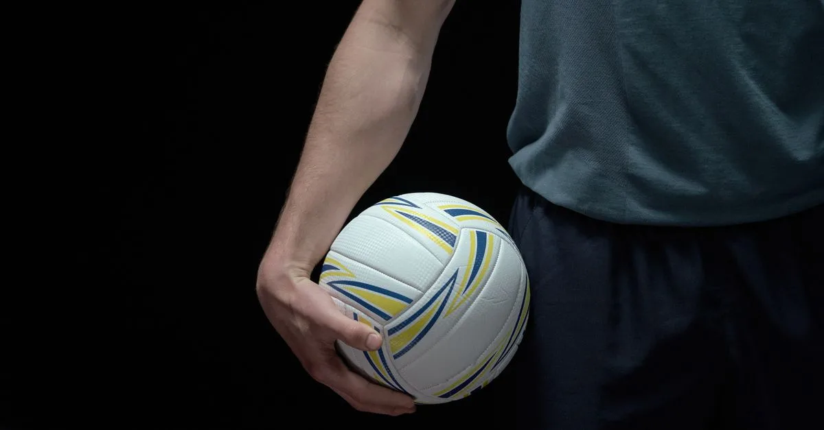 Close-up shot of a volleyball held by a person against a dark background, emphasizing sports readiness.