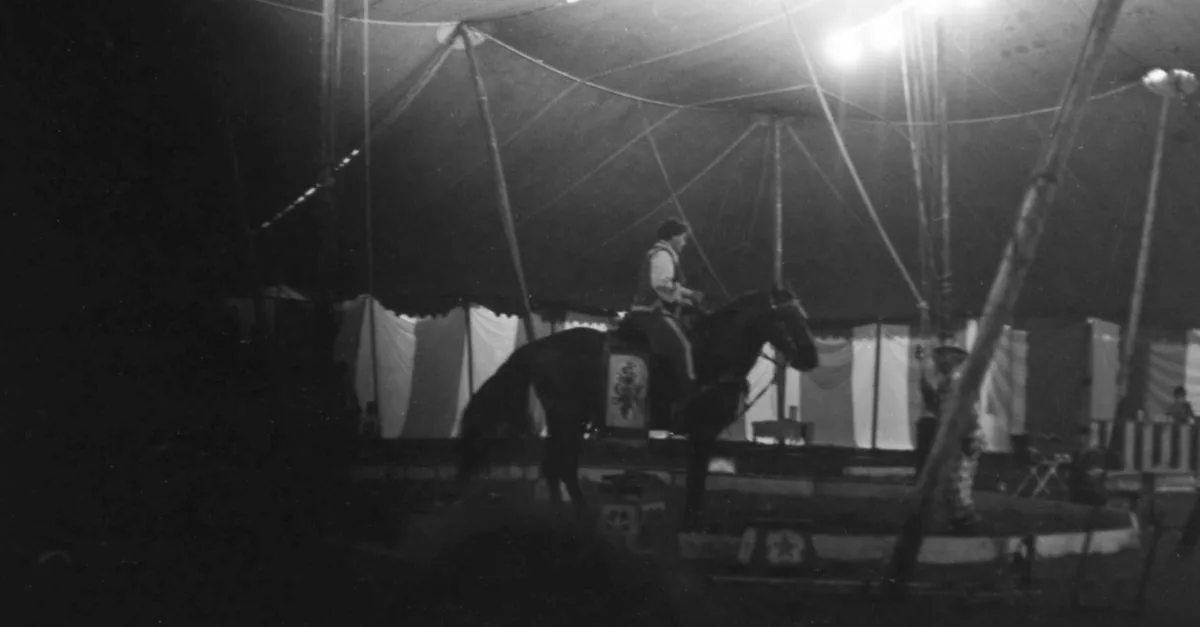 Grayscale image of a horseback performance inside a circus tent.