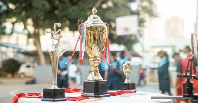 A golden trophy displayed on a table during an outdoor sports event with blurred players in the background.