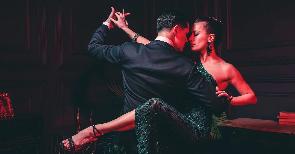 A couple elegantly dancing with intense passion under red lighting, showcasing intimacy and glamour.