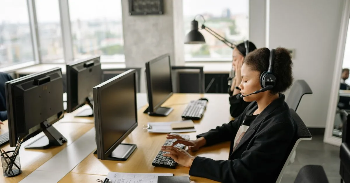 Customer support agents working at a call center with computers and headsets, focusing on tasks.