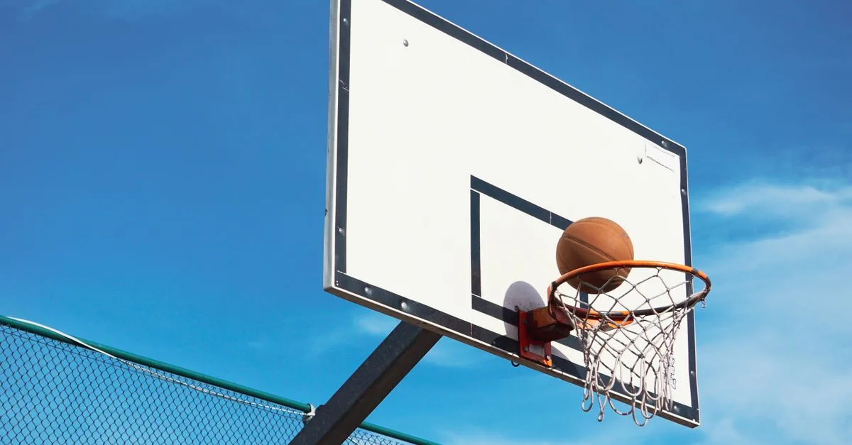 A basketball scoring shot on an outdoor court with a clear blue sky backdrop.