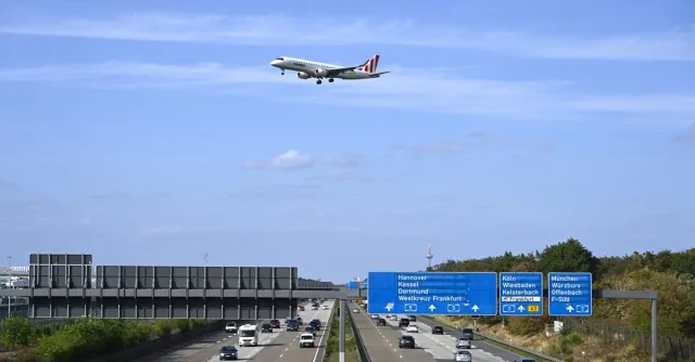 Passenger airplane flying over highway near Frankfurt, Germany, with clear sky background.