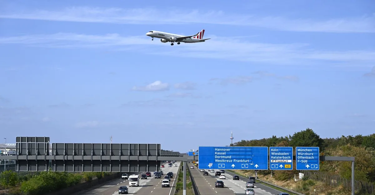 Passenger airplane flying over highway near Frankfurt, Germany, with clear sky background.