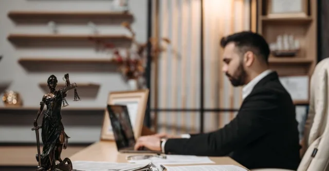 Lawyer working diligently on a laptop in a modern office, Lady Justice statute present.