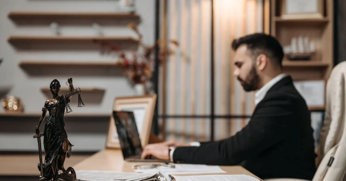 Lawyer working diligently on a laptop in a modern office, Lady Justice statute present.