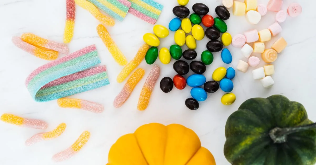 Vibrant assortment of Halloween candies and mini pumpkins, perfect for festive decoration.