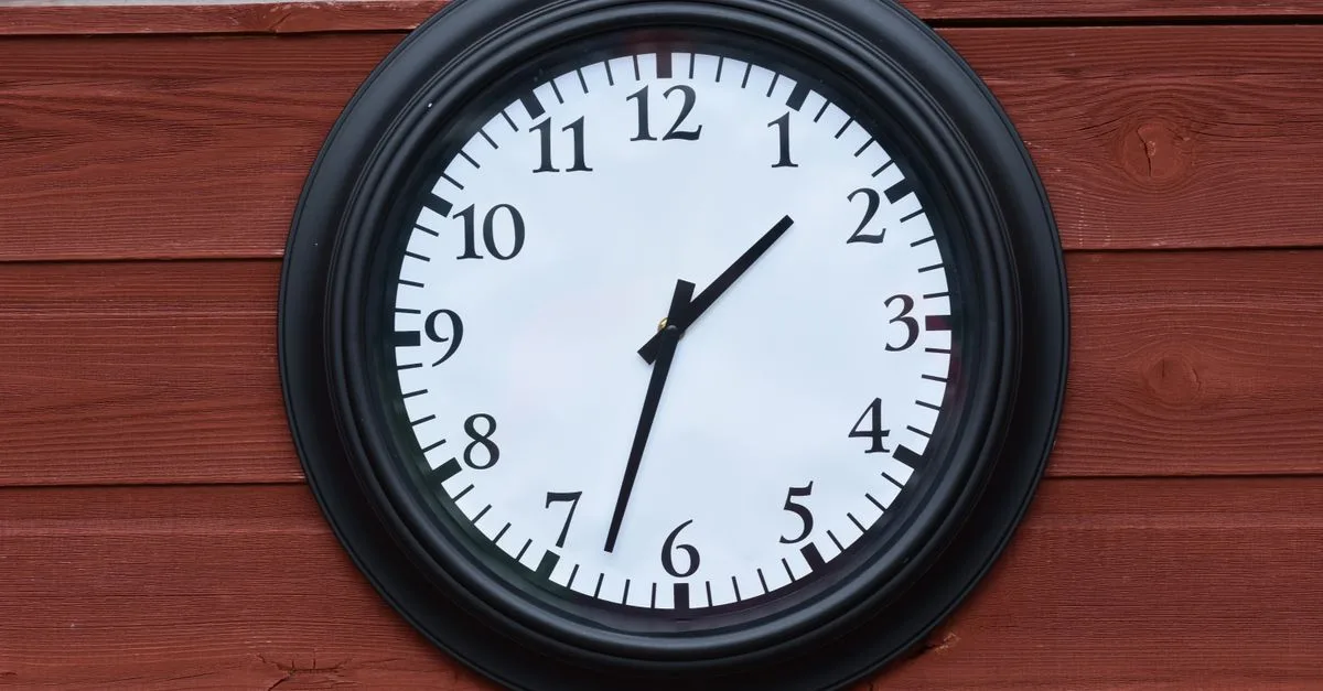 Close-up of a black round wall clock mounted on a rustic wooden wall.