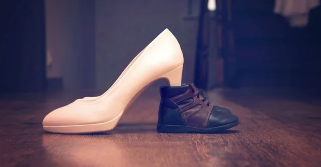 A compelling juxtaposition showcasing an adult high heel and a baby shoe side by side on a wooden floor.