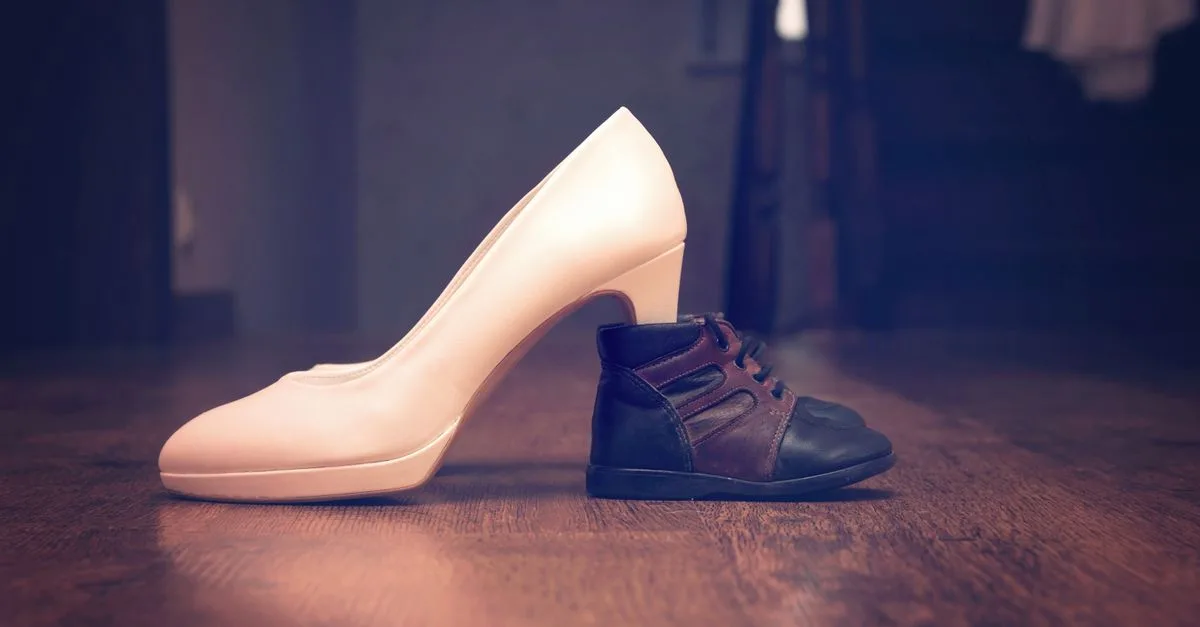 A compelling juxtaposition showcasing an adult high heel and a baby shoe side by side on a wooden floor.