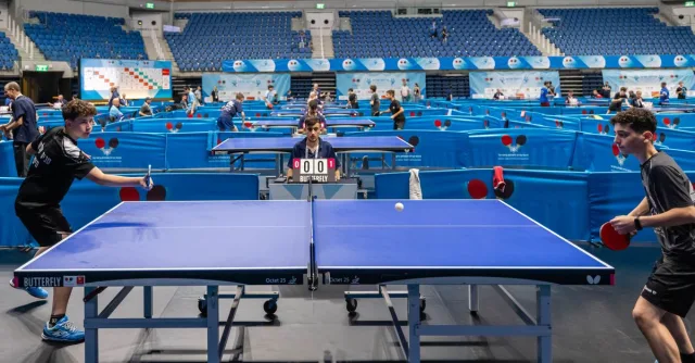 Players compete in a lively table tennis tournament in a large indoor stadium.