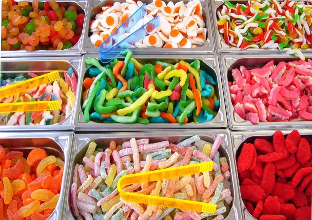 A close-up of colorful fruit-shaped gummy candies in a clear plastic bag on a neutral background.