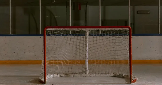 A still shot of an ice hockey rink featuring an empty goal net and puck on the ice.