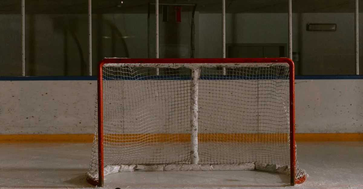 A still shot of an ice hockey rink featuring an empty goal net and puck on the ice.