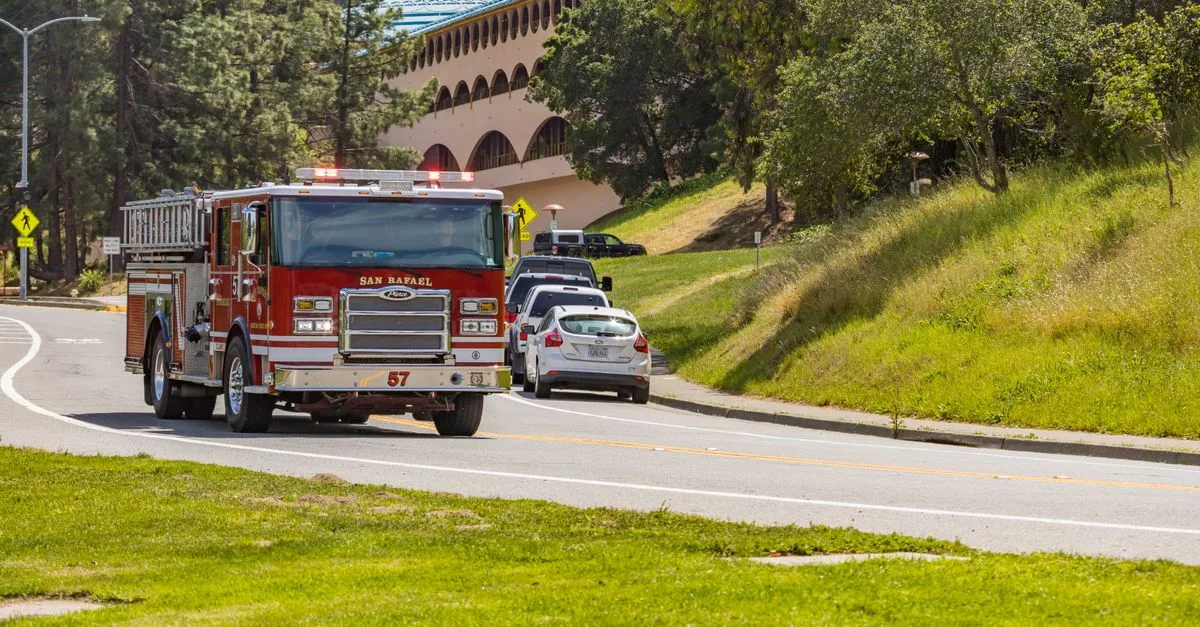 Red fire truck on a curvy road surrounded by lush greenery near a San Rafael landmark.