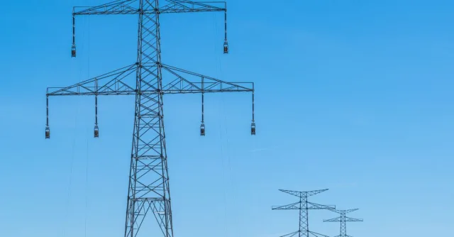 Blue sky over transmission towers on a rural landscape, symbolizing energy distribution.