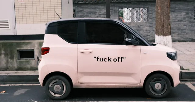 Side view of a pink compact electric vehicle parked on an urban street with bold text on the side.