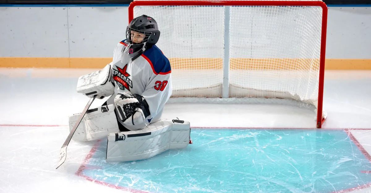 Ice hockey goalie in full gear kneeling on the ice to defend the goal.