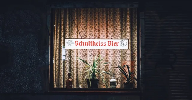 Cozy Berlin pub window display with illuminated sign and plants at night.